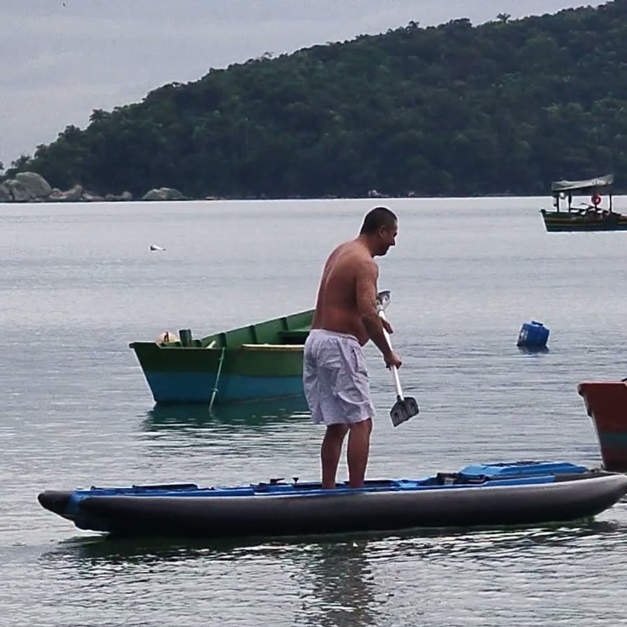 Caiaque com flutuador inflável visto de lado no mar, pessoa em pé com remo
